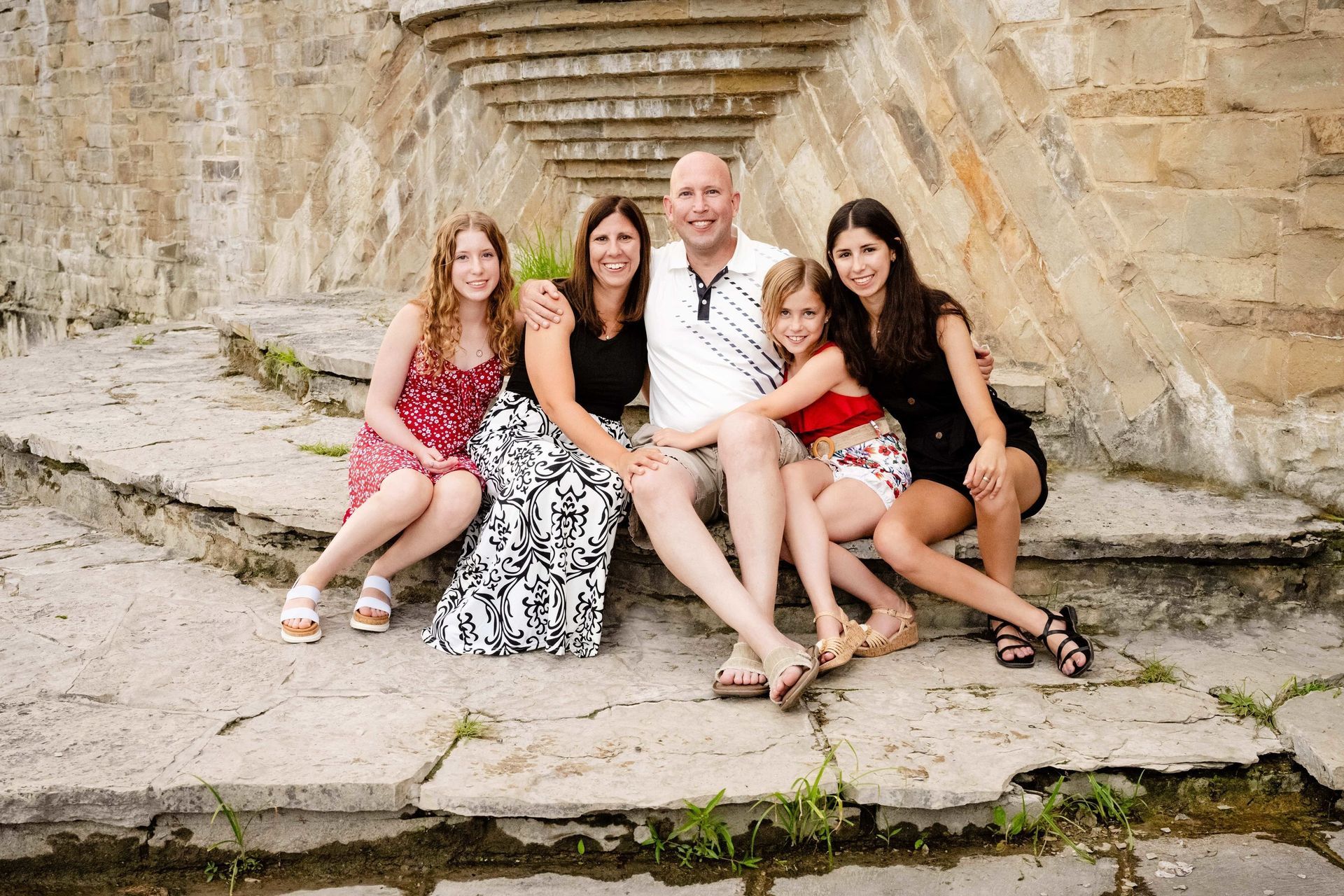 Family of five sitting on stone steps; smiling at the camera.
