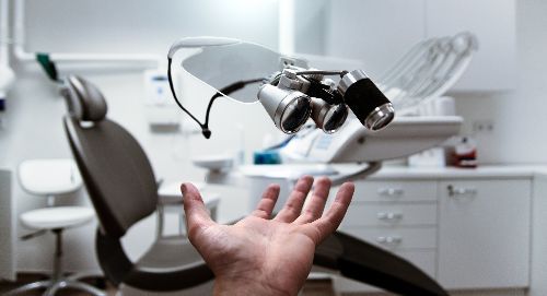 Hand reaching toward dental equipment in a clean, white dentist's office with a chair, and cabinets.