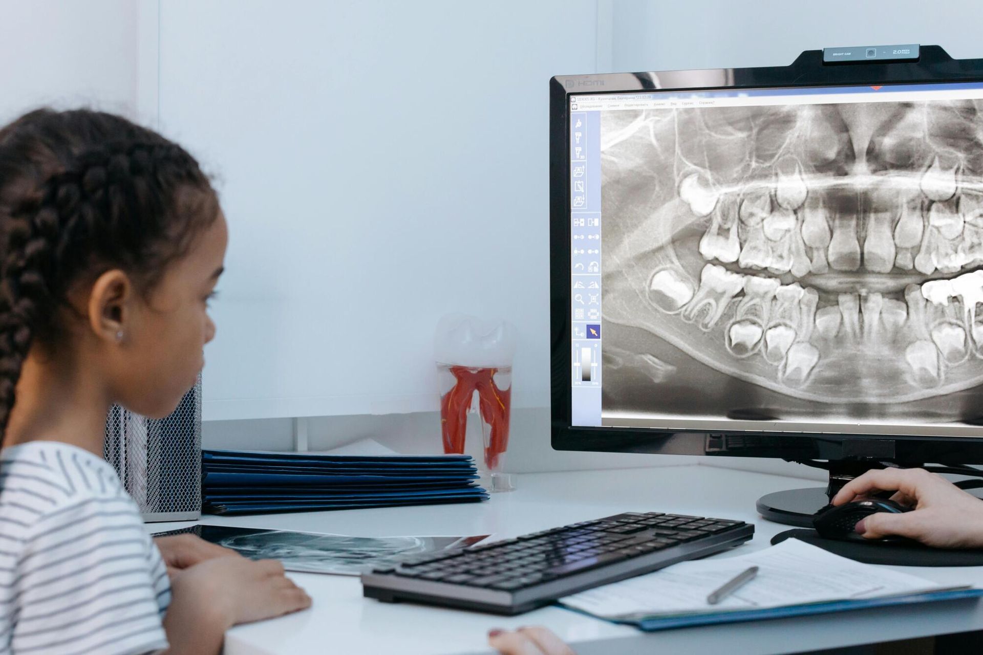 Child viewing dental X-ray on a computer at a desk with a dentist’s workstation nearby