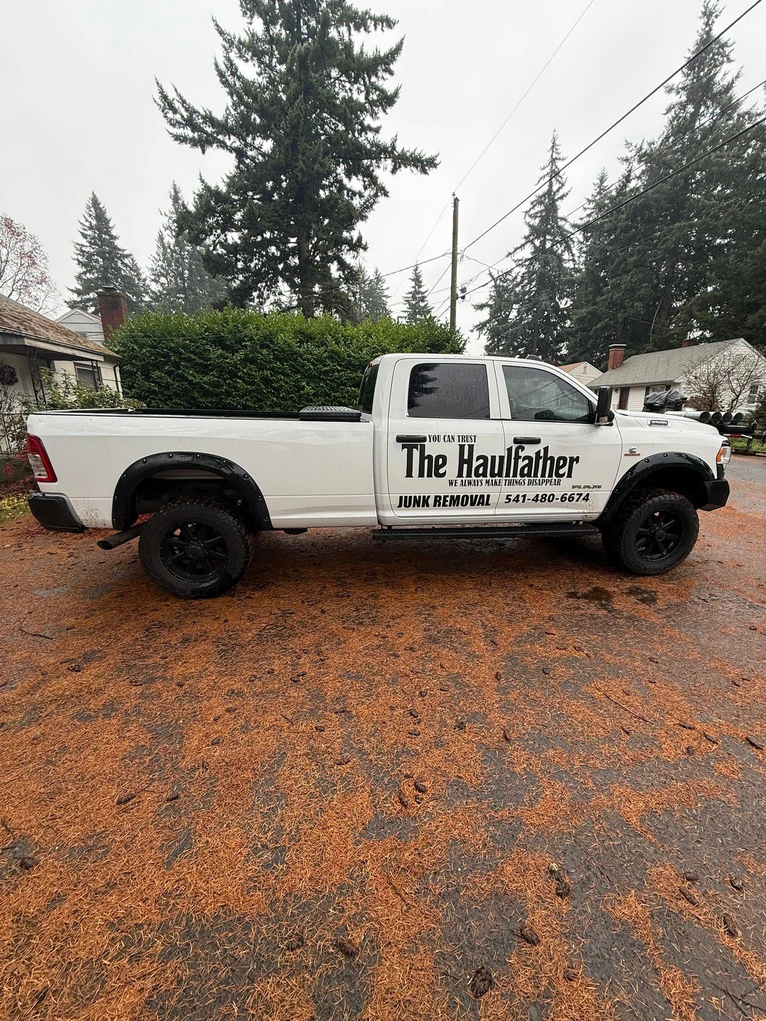 White pickup truck with “The Paul…” logo parked on a wet, gravel driveway in a rainy, wooded area