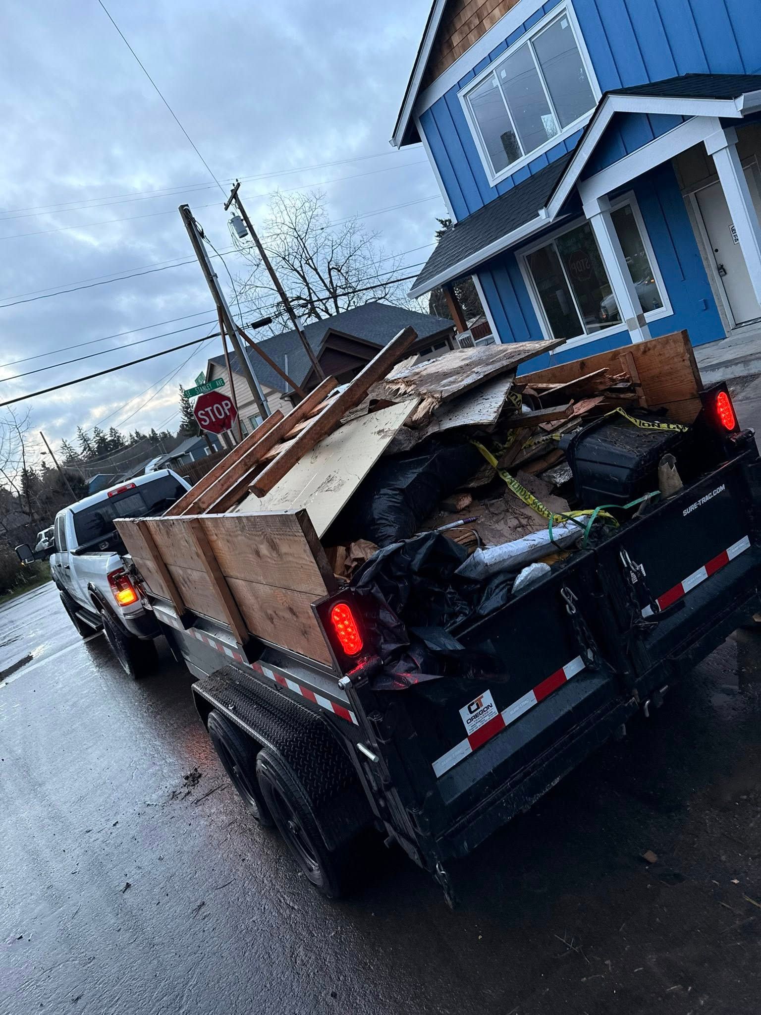 Pickup truck loaded with debris parked beside a blue house on a wet street.