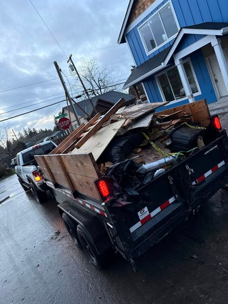 Pickup truck loaded with debris parked beside a blue house on a wet street.