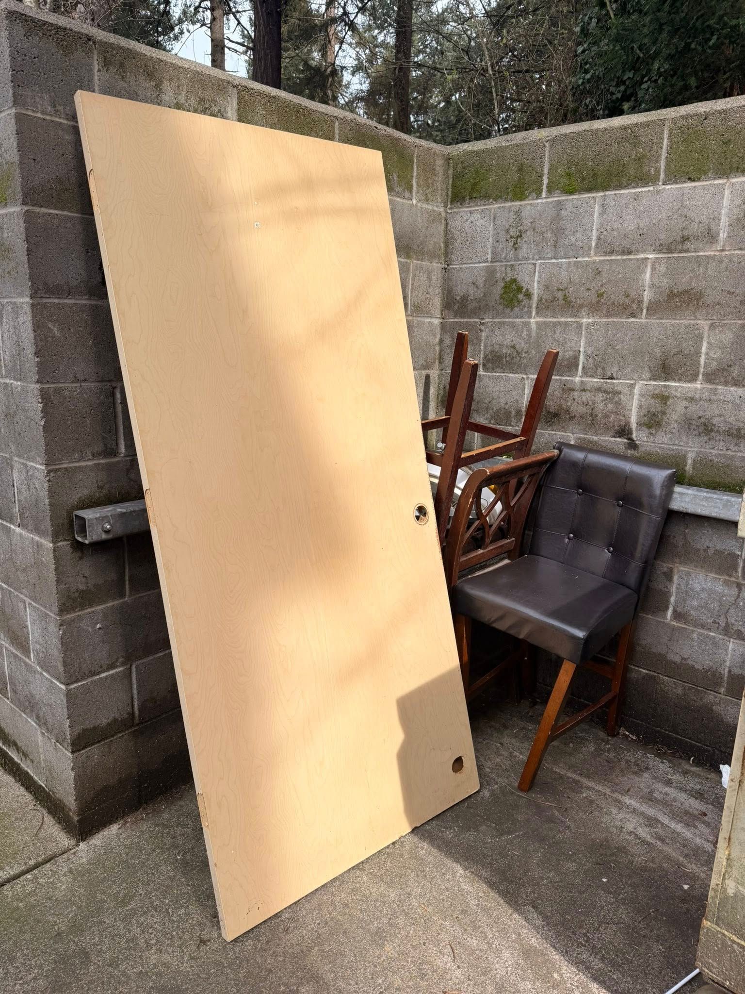 Large beige panel leaning against cinderblock walls beside stacked outdoor chairs in a small yard.