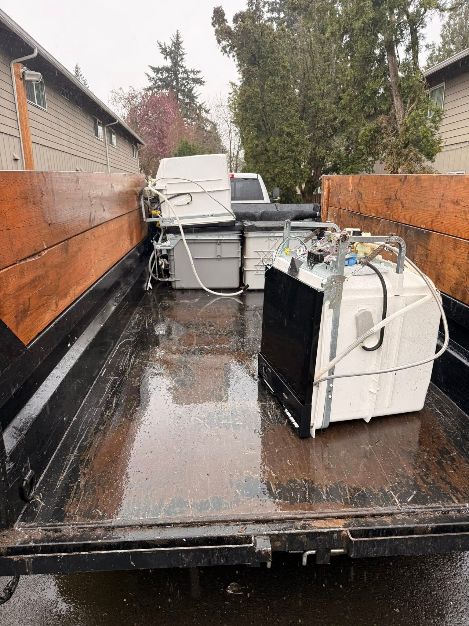 Wet pickup truck bed loaded with large white appliances on a rainy day