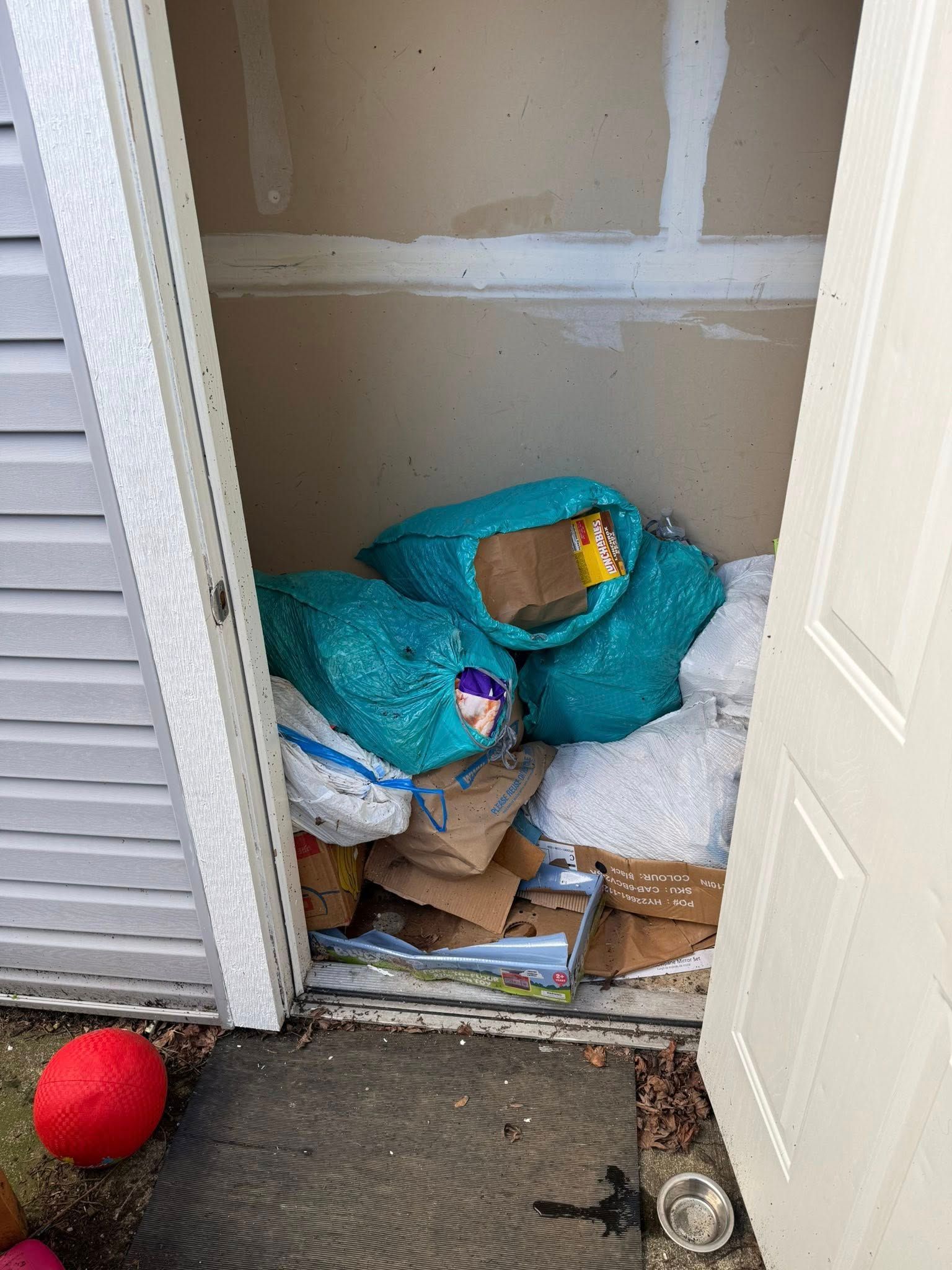 Closet stuffed with bags, boxes, and clutter; red ball on the floor outside.