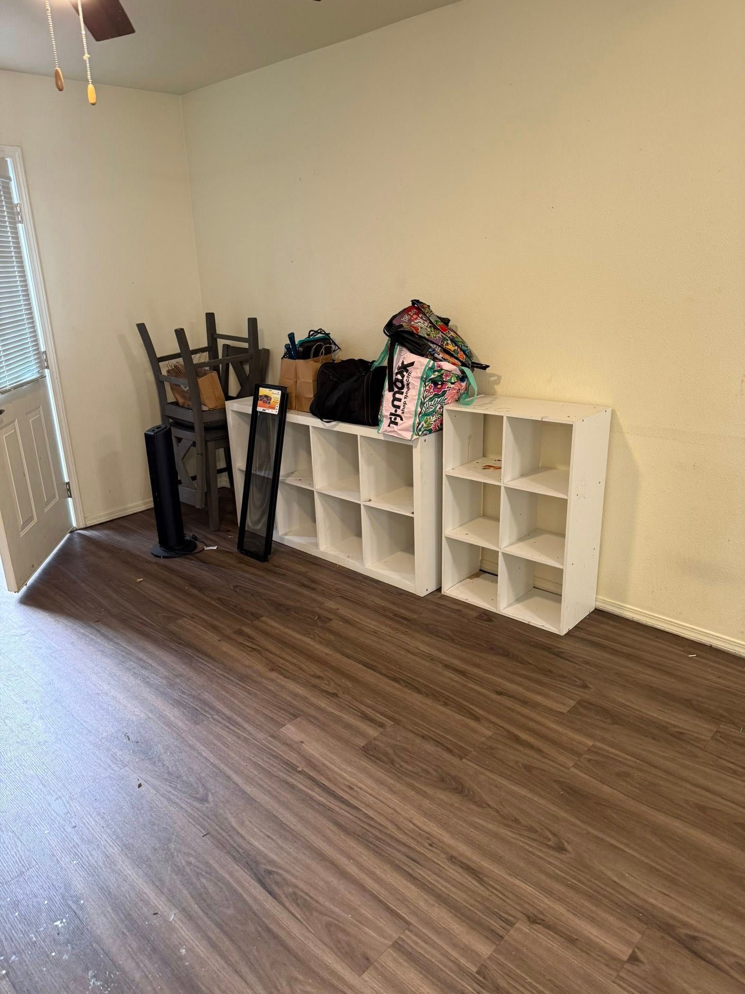 Empty room with wood flooring, white cubbies, folded chairs, and a bag against a beige wall.