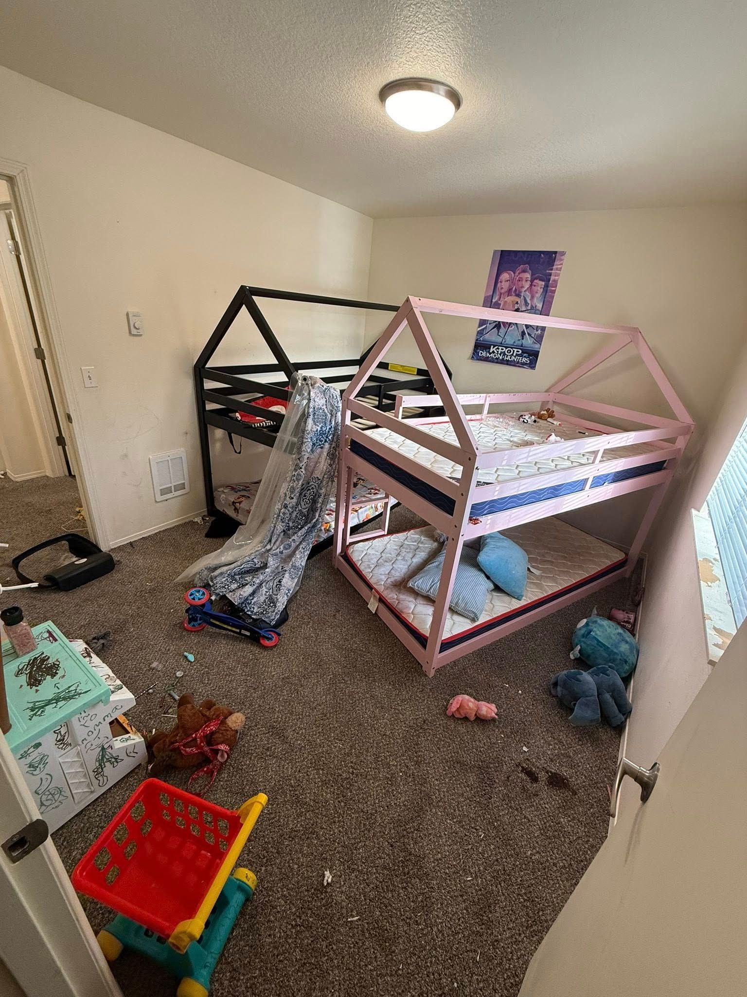 Children’s playroom with two small house beds, toys, and a carpeted floor.