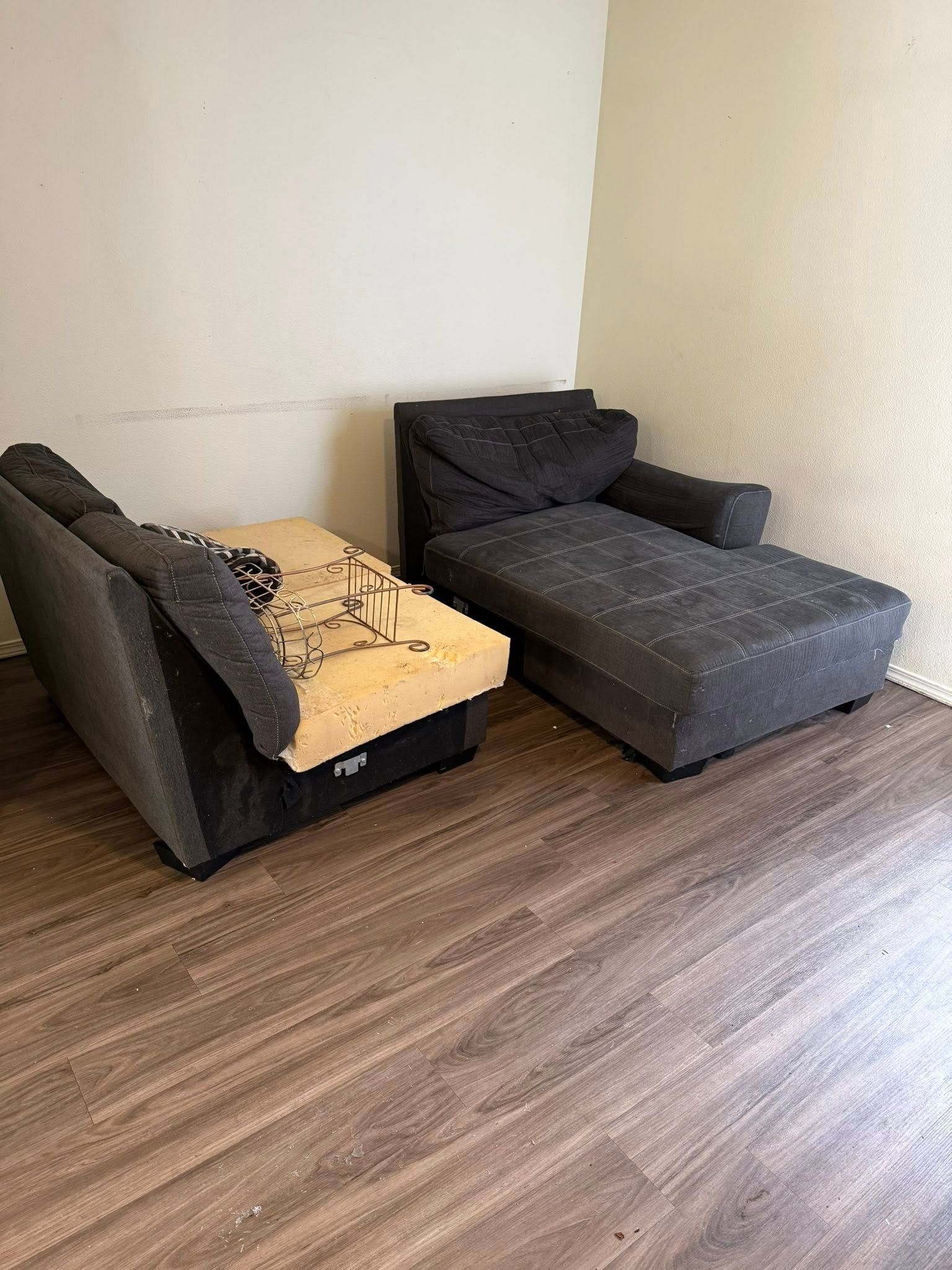 Two dark gray chaise sofas in a corner room with wood flooring and beige walls