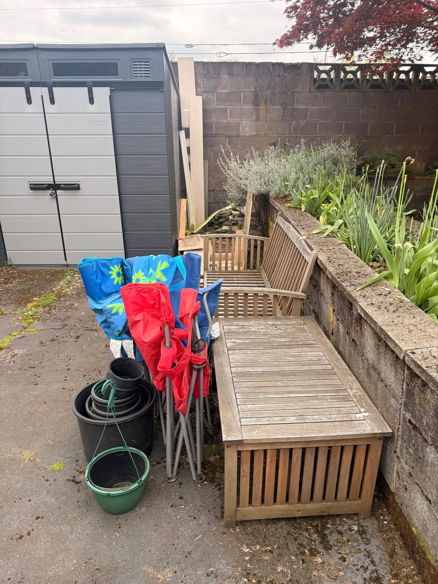 Backyard patio with folded umbrellas, green pots, and a wooden bench beside a fence and shed