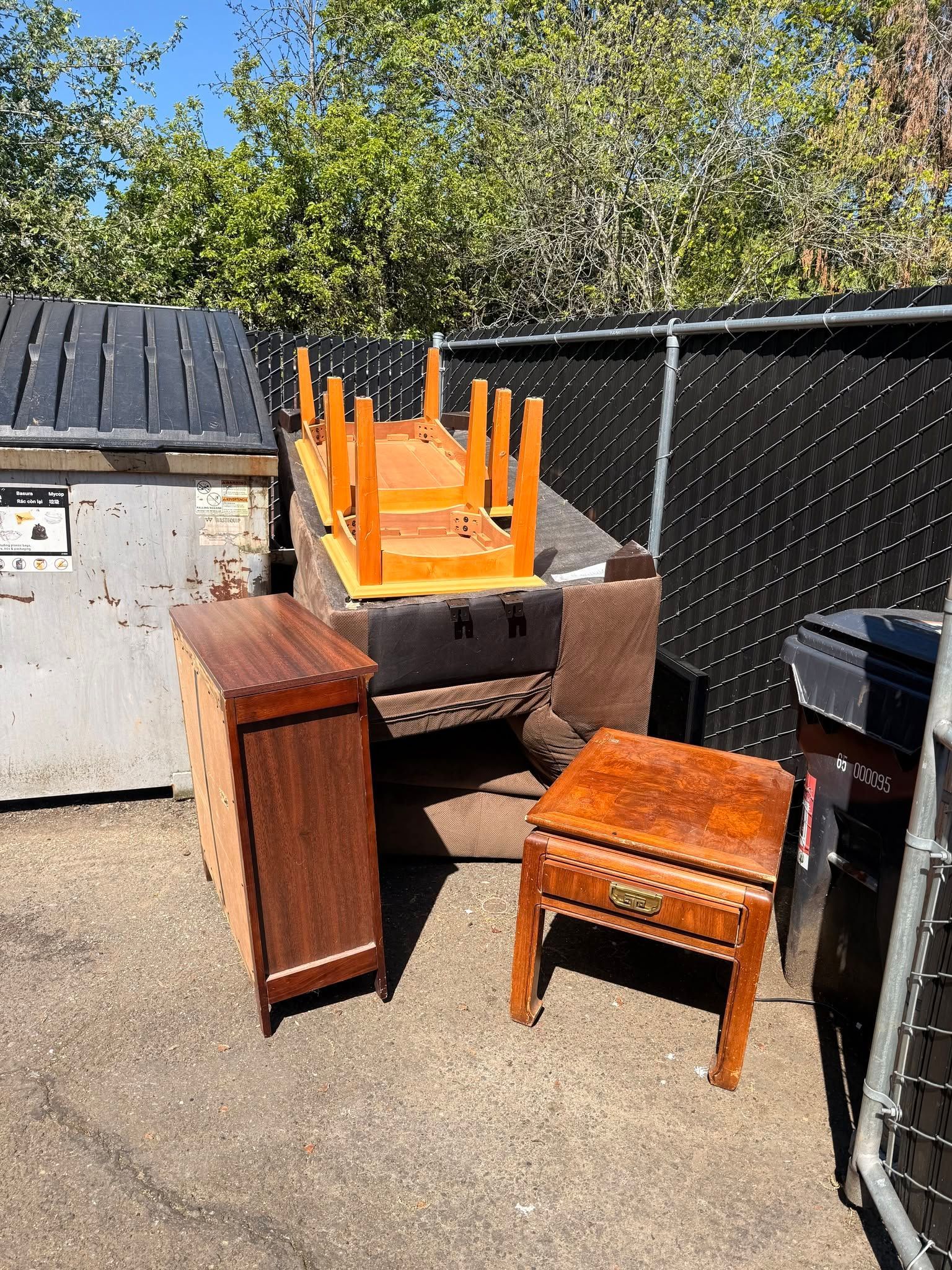 Outdoor yard with stacked orange chairs on a grill, beside a wooden cabinet and small stool by a fence.