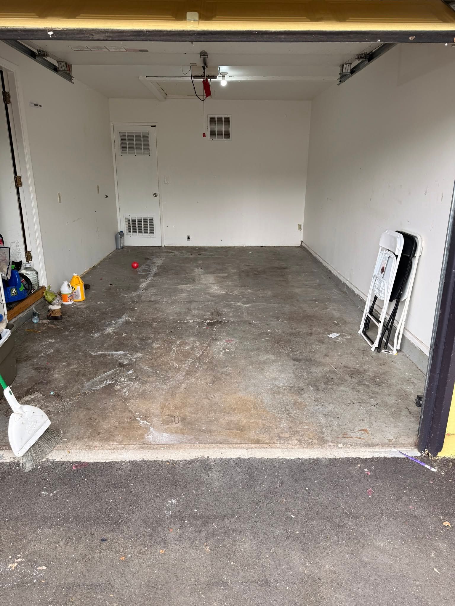 Empty garage with white walls, concrete floor, and scattered cleaning supplies near the entrance