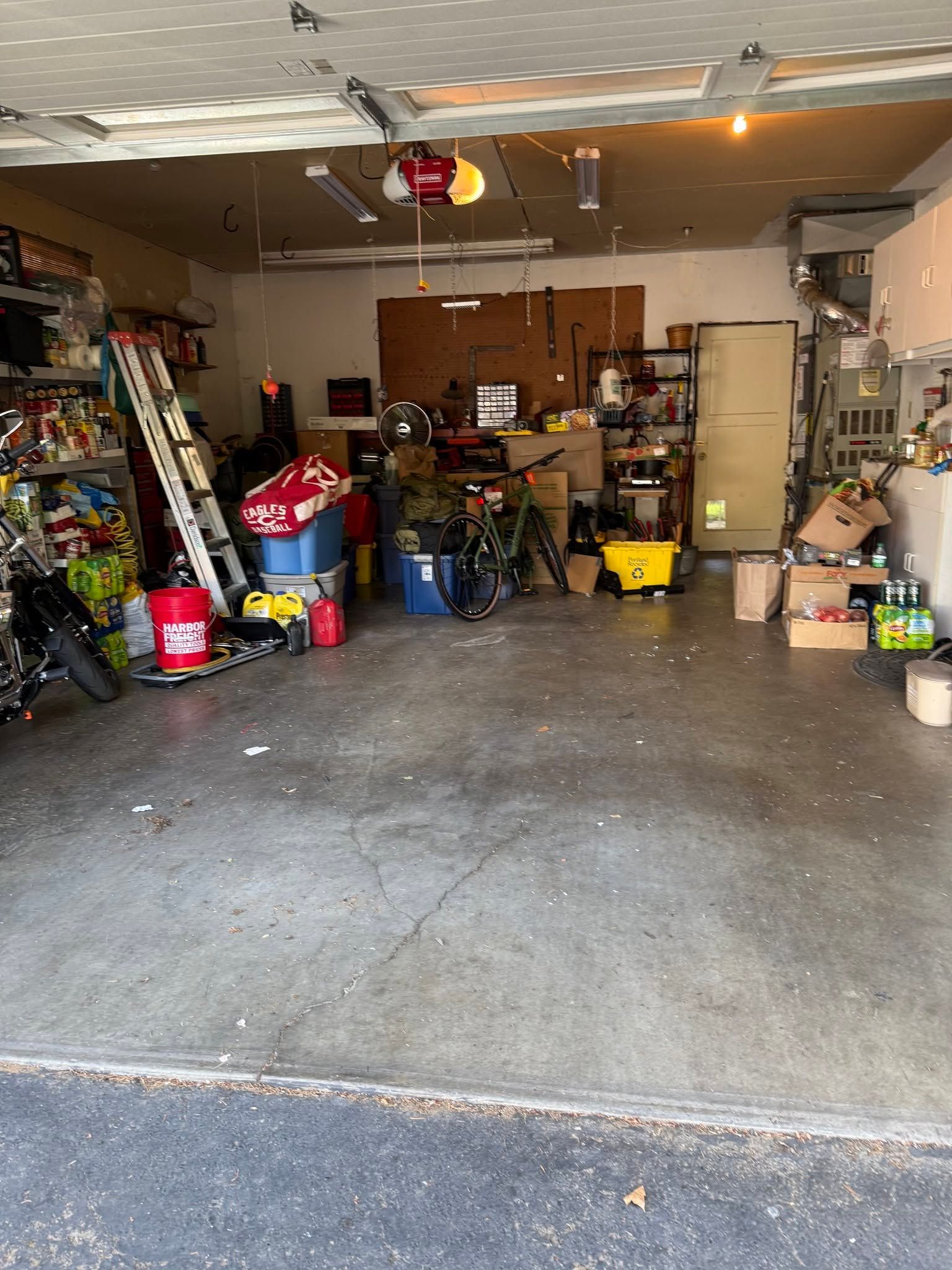 Cluttered garage with tools, storage bins, and supplies on shelves and the floor