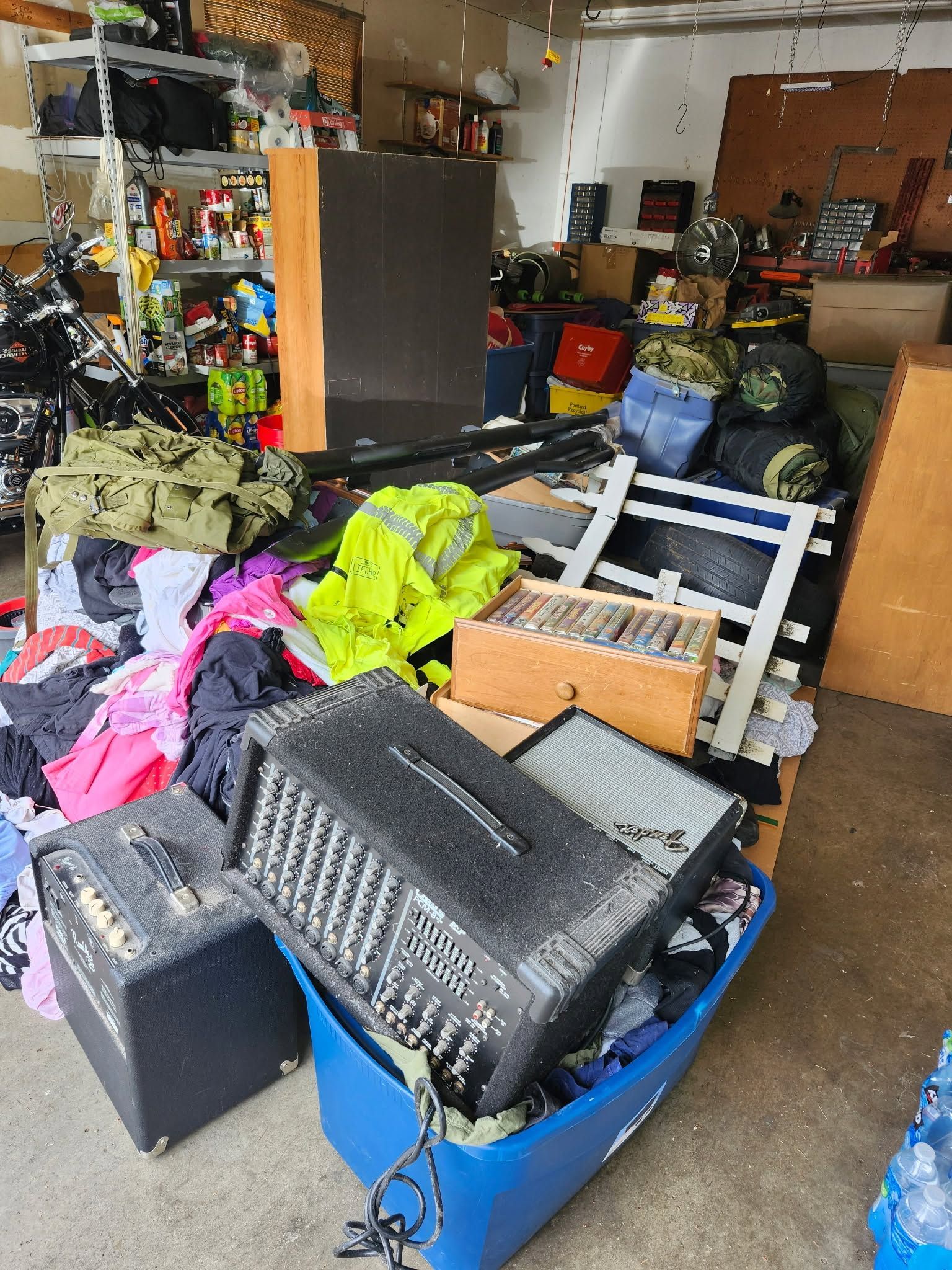 Cluttered garage packed with bins, tools, jackets, and equipment, with a blue storage tote in front