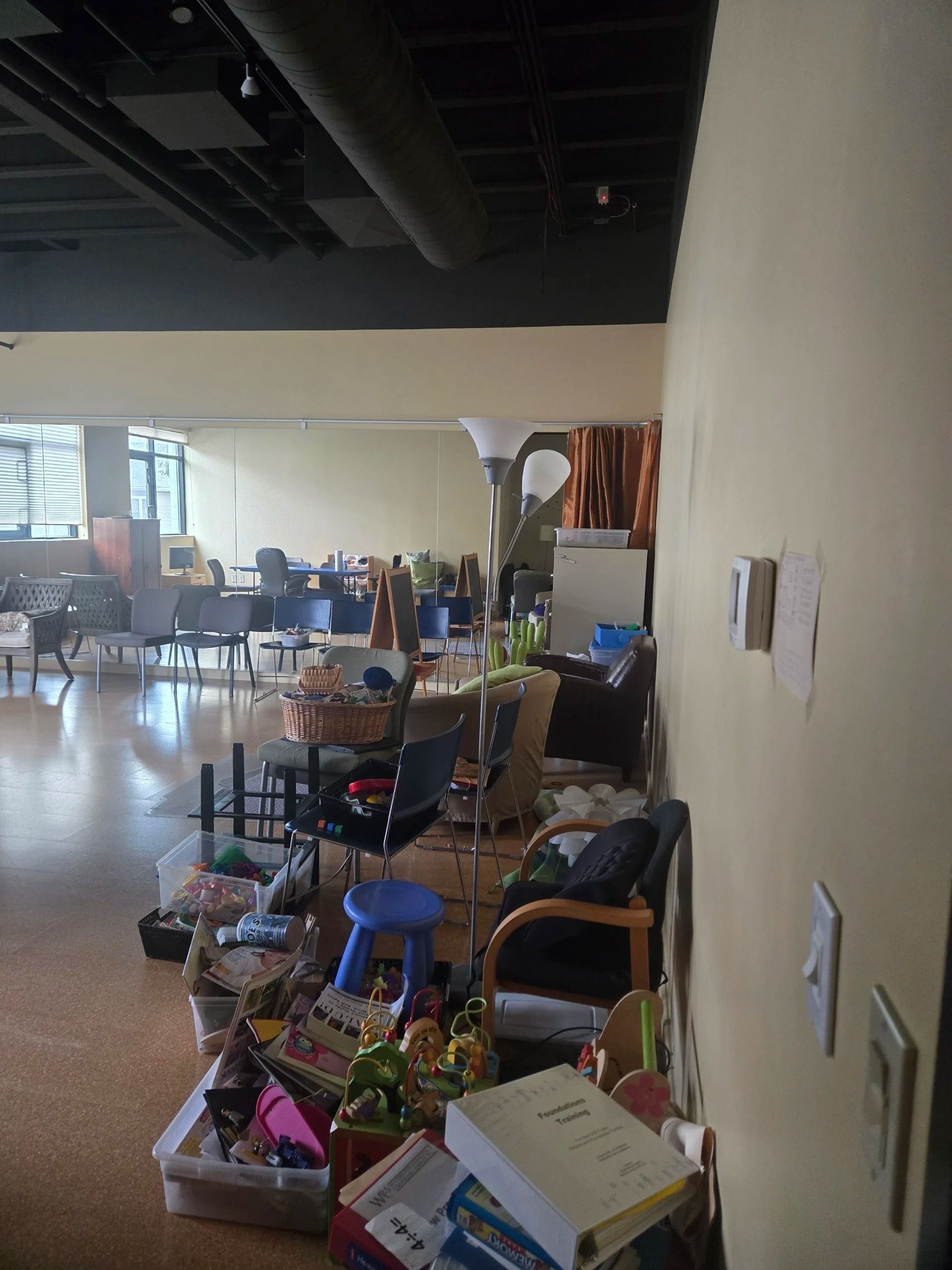 Indoor hallway with chairs and boxes lined against a wall in a cluttered office or common area
