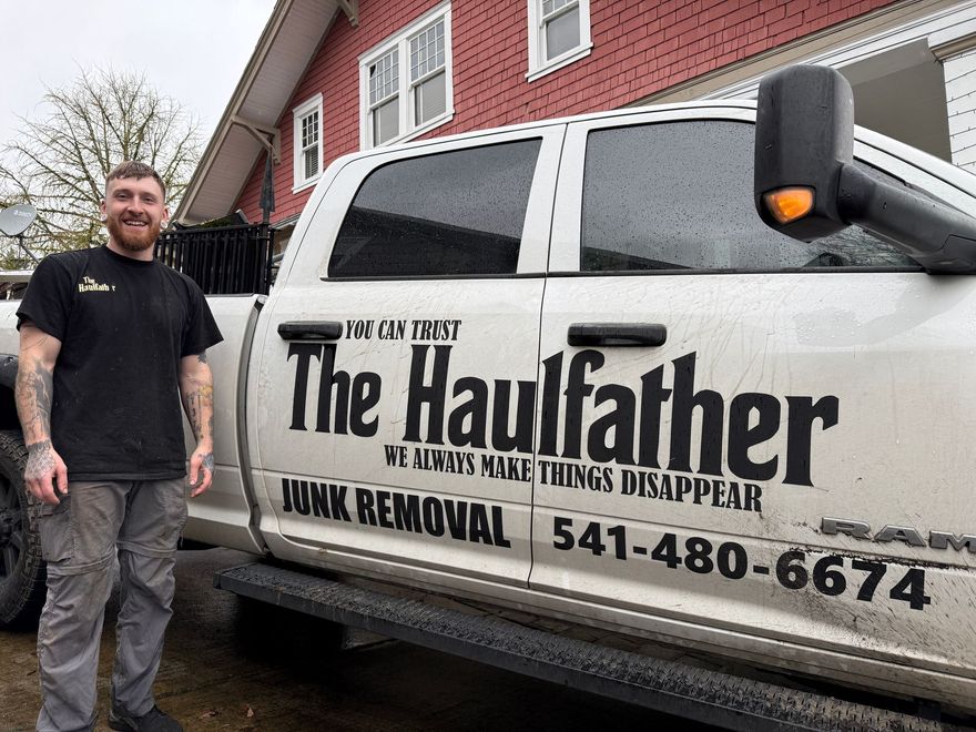 Man standing beside white Haulfather junk-removal truck parked by a red building