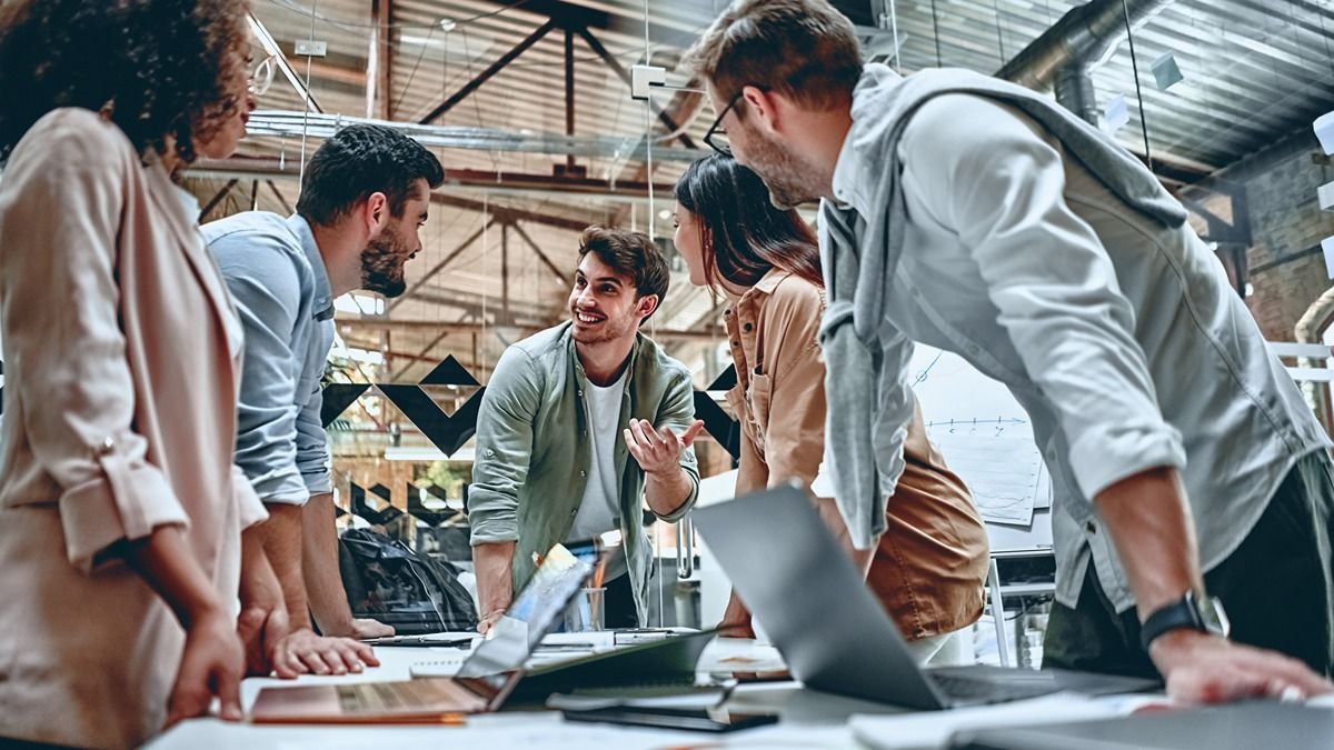 A group of people are standing around a table looking at a laptop.