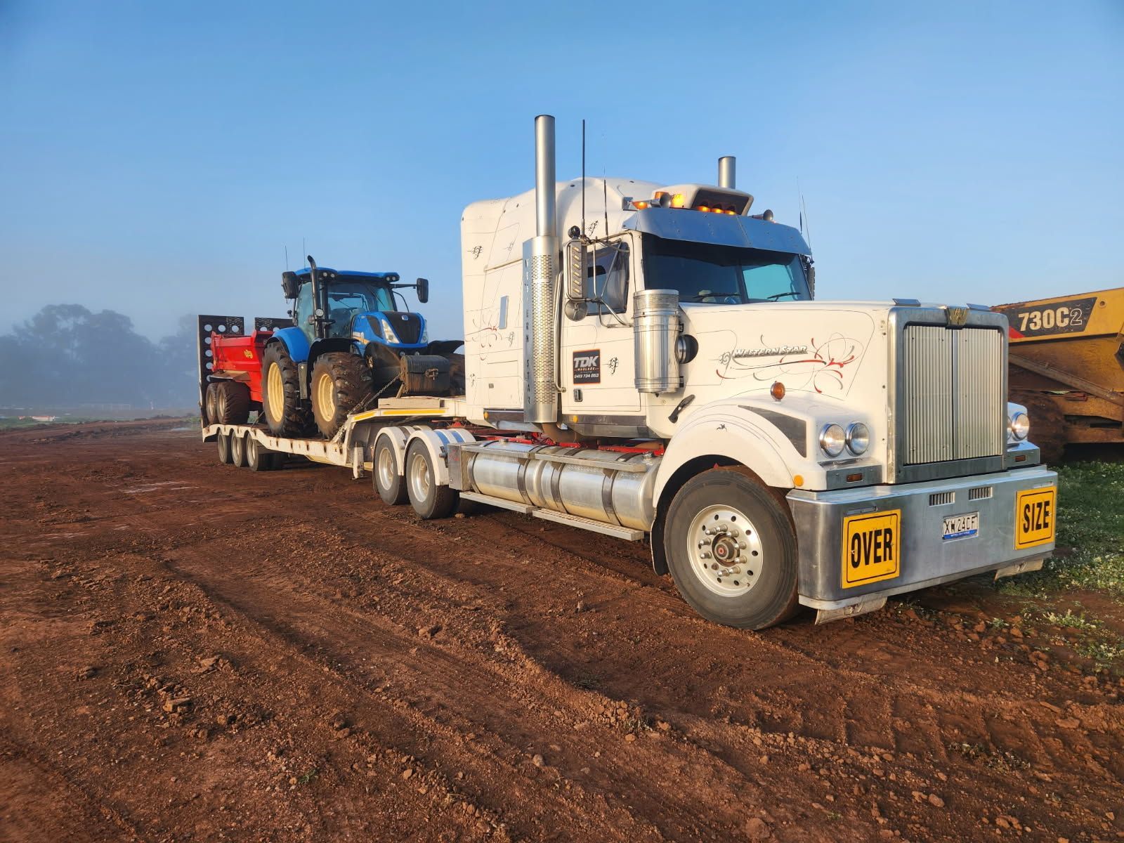 White semi-truck hauling equipment on a muddy dirt road in a rural field