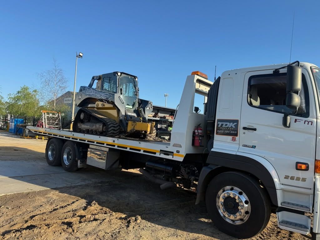 Flatbed tow truck carrying a yellow construction loader on a sunny roadside.