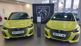 Two yellow Peugeot cars displayed indoors with a Peugeot sign between them