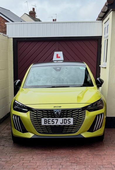 Yellow car with learner sign parked in a driveway in front of a garage