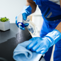 Blue-gloved cleaner spraying disinfectant onto a cloth on a countertop