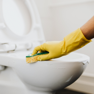 Gloved hand scrubbing a white toilet bowl with a sponge