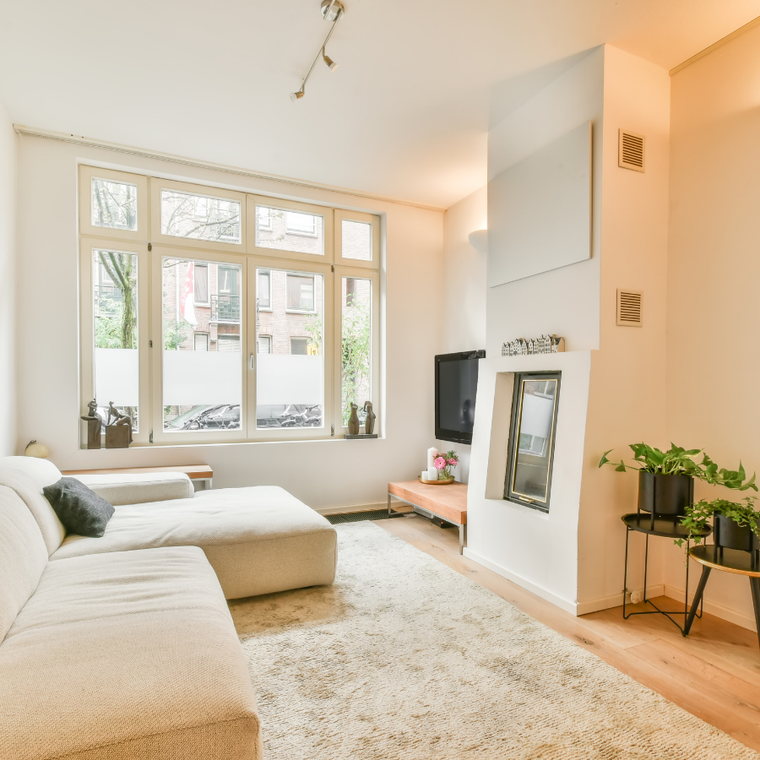Bright living room with white sectional sofa, large windows, fireplace, and potted plants