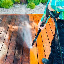Person pressure washing a wooden deck, with a clean section beside a dirty one.
