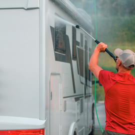 Person pressure-washing a white RV with a long wand, spraying water along the side panel.