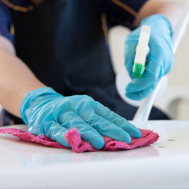 Gloved hands cleaning a white surface with pink cloth and spray bottle