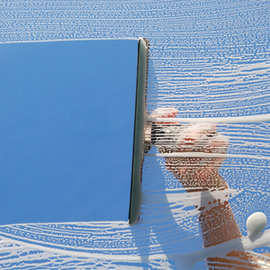 Hand wiping a blue glass panel with a squeegee, leaving clean streaks on the surface.