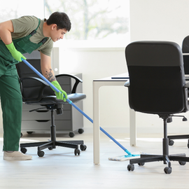 Person cleaning an office floor with a blue mop beside desks and chairs
