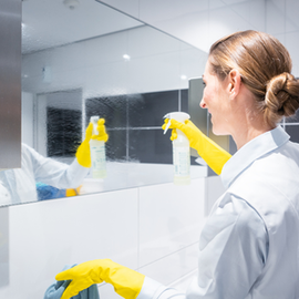 Lab worker in white coat and yellow gloves cleaning a mirrored wall in a bright laboratory