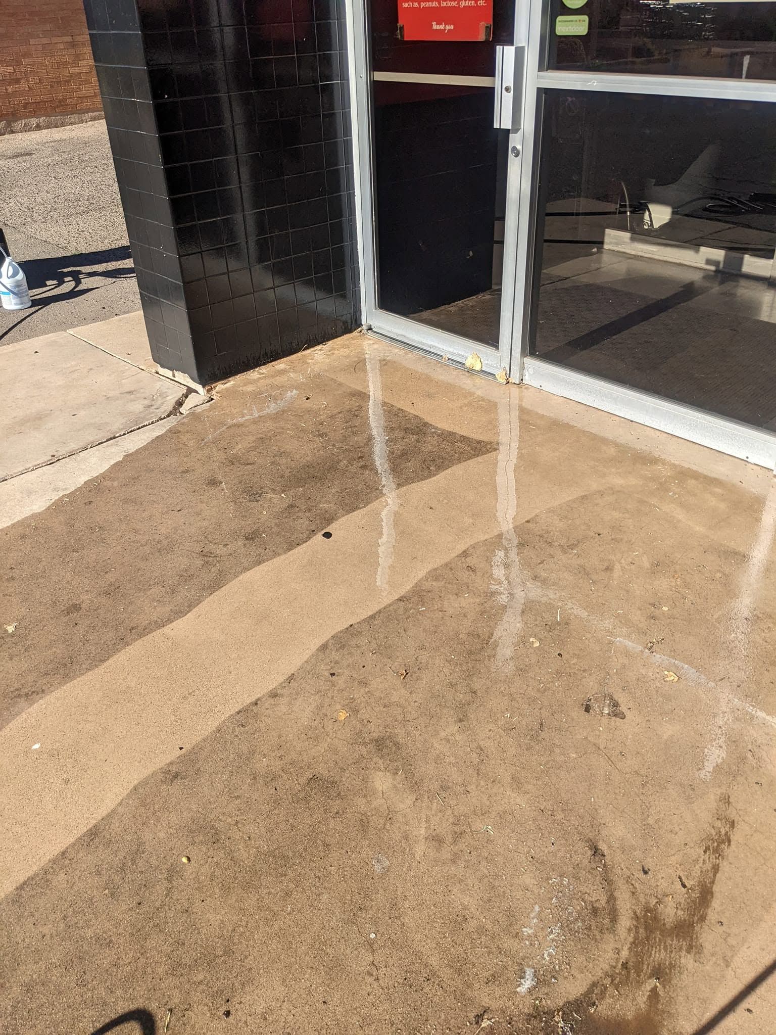 Water streaming down a storefront sidewalk beside glass doors and a brick wall