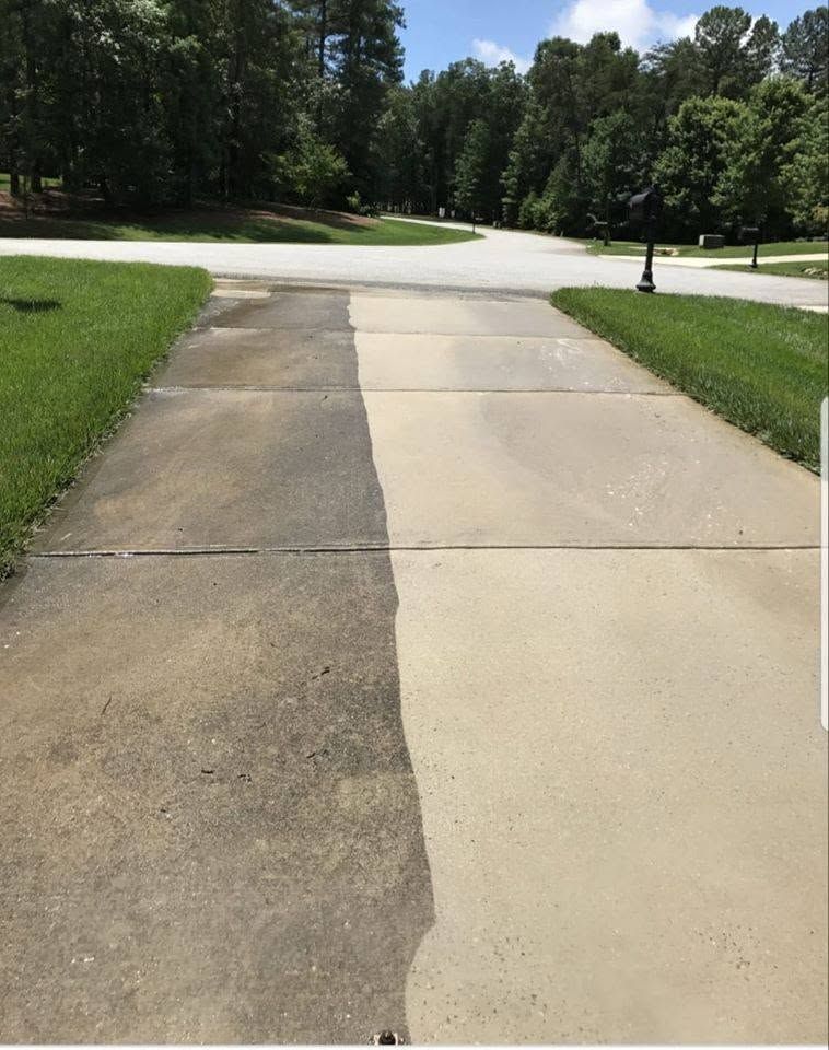 Concrete driveway leading to a street, bordered by green lawns and trees on a sunny day