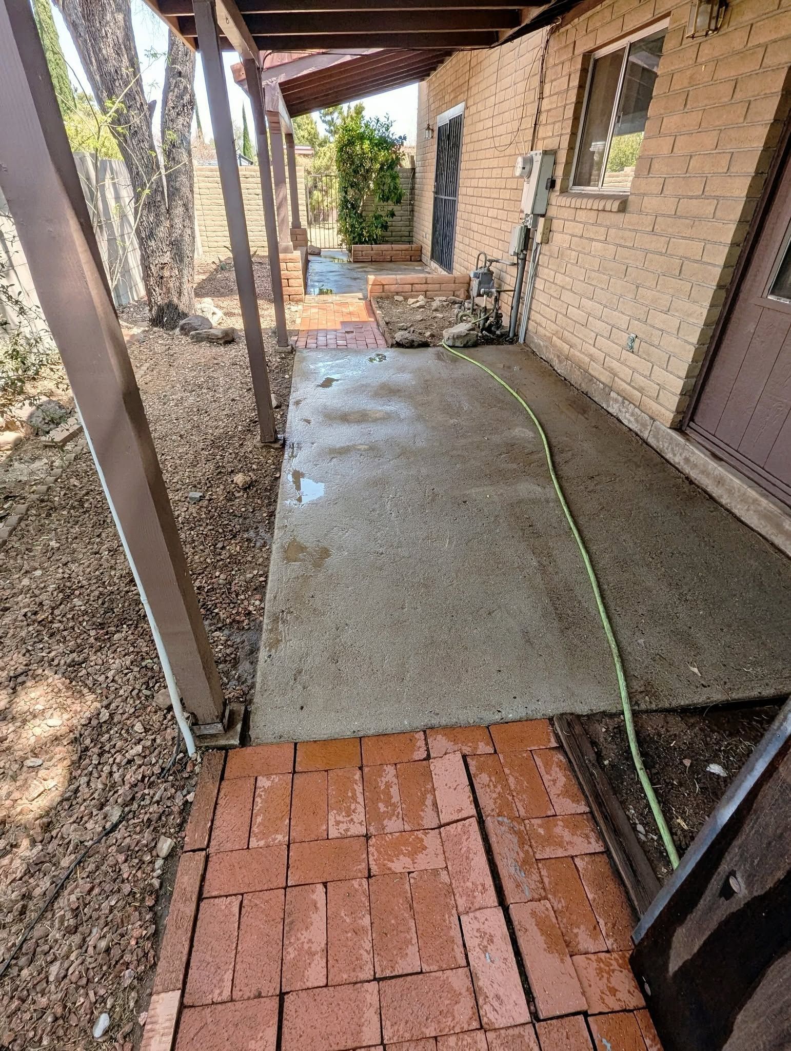 Narrow brick and concrete walkway beside a house, with a screened porch on the left and brick wall on the right.