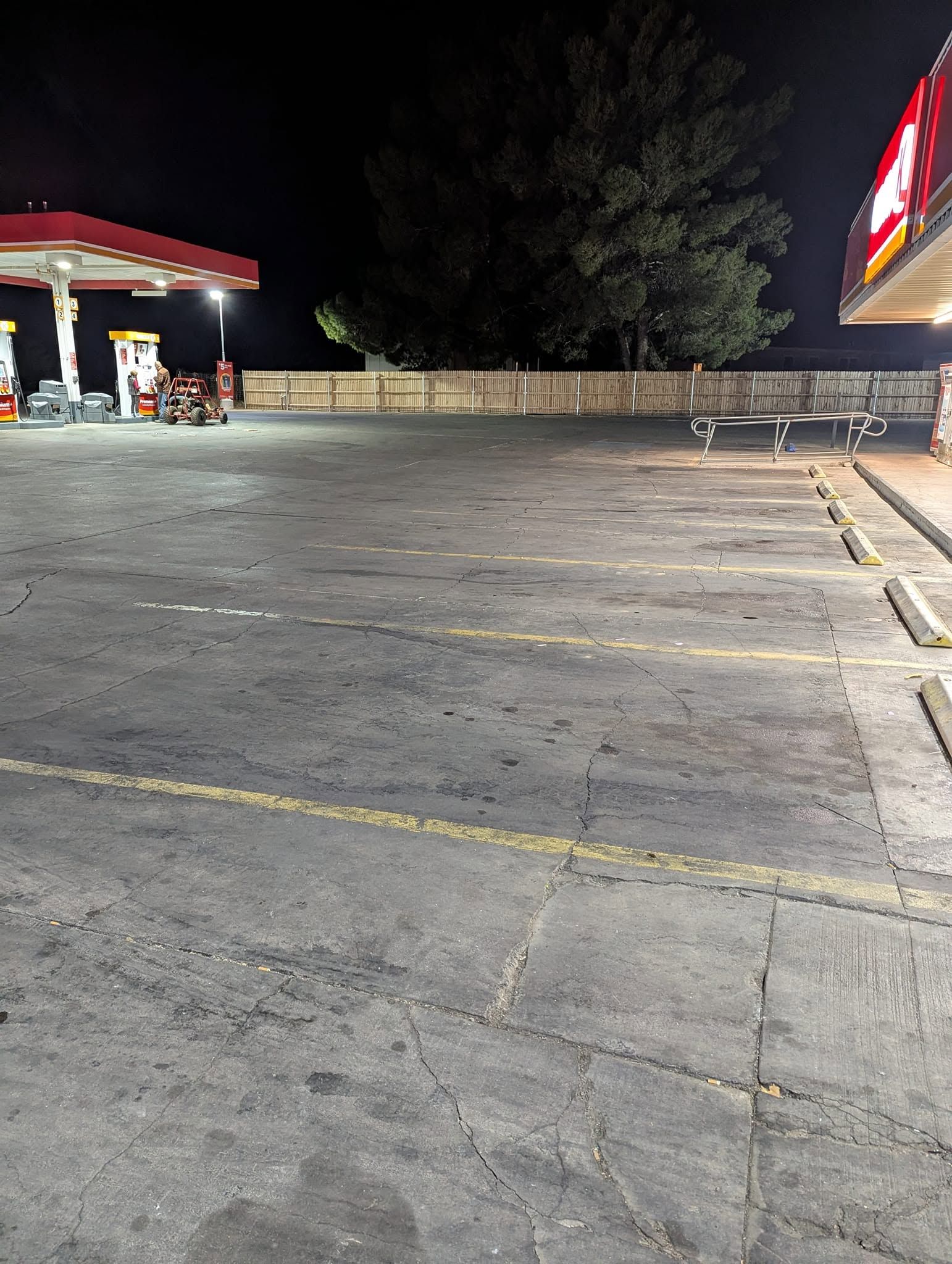 Empty gas station parking lot at night, with a lit canopy and red-striped building edge.