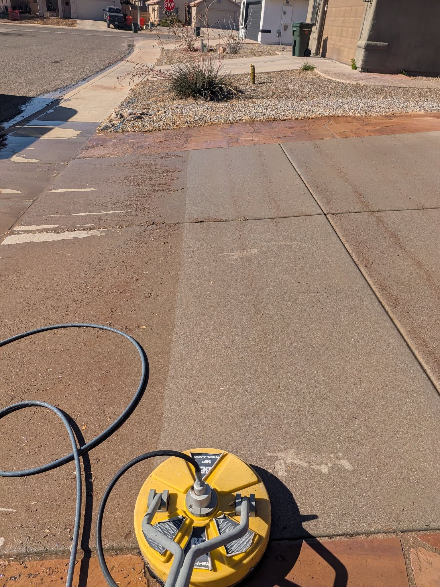 Yellow sewer camera on a long black cable on a sunlit paved road near a gravel mound and buildings
