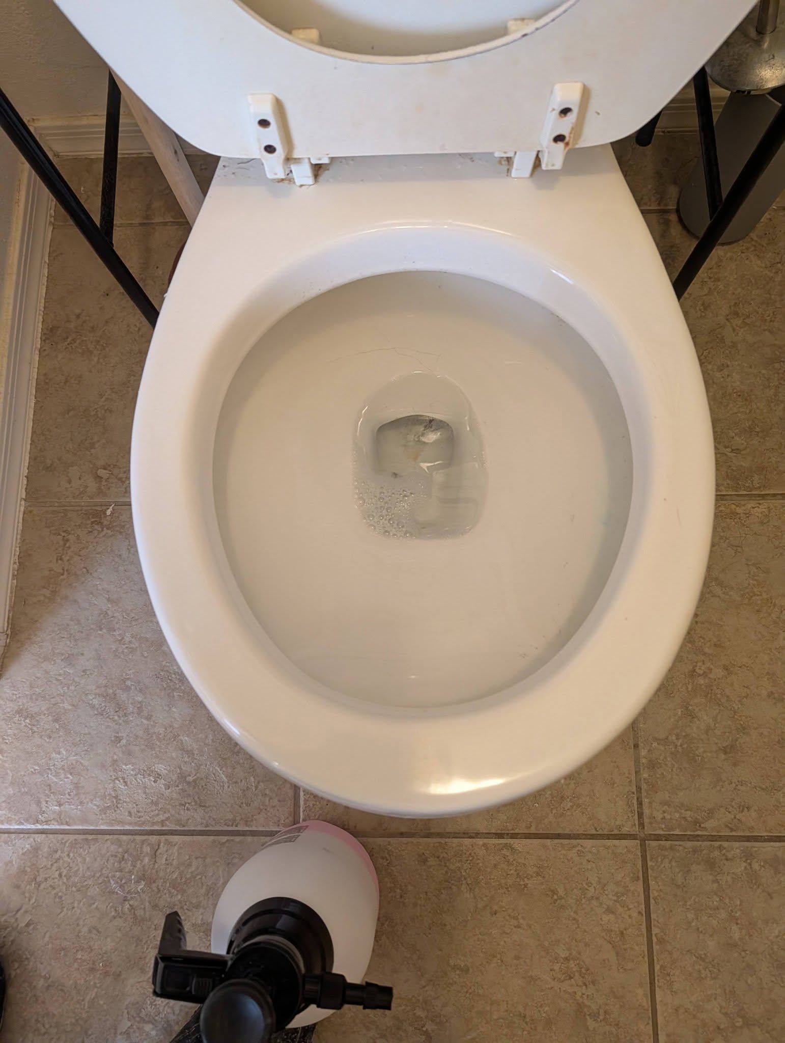 Open toilet with water; toilet paper roll visible on the bathroom floor.