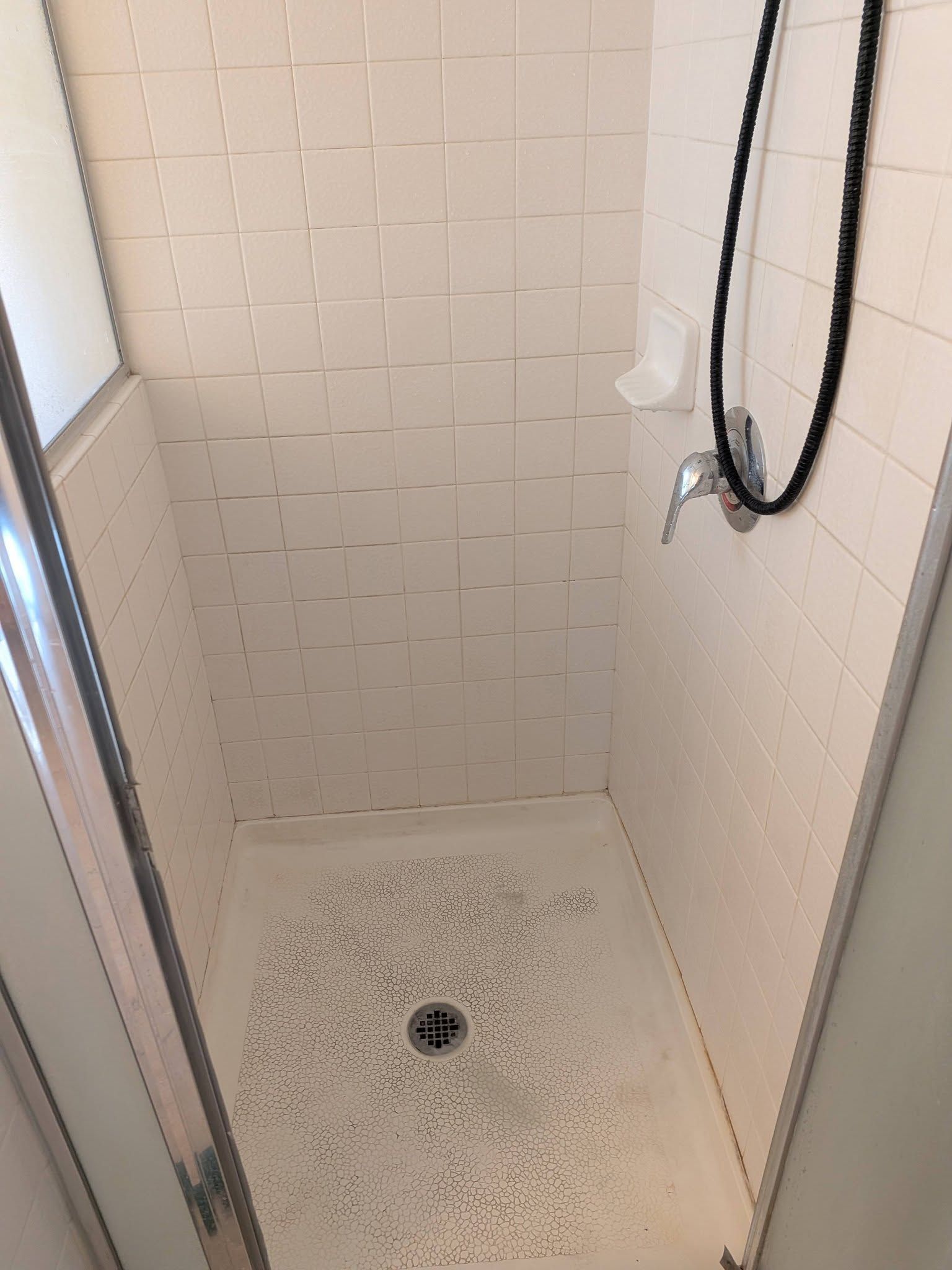 Small tiled shower stall with a drain, handheld shower hose, and soap residue on the floor.