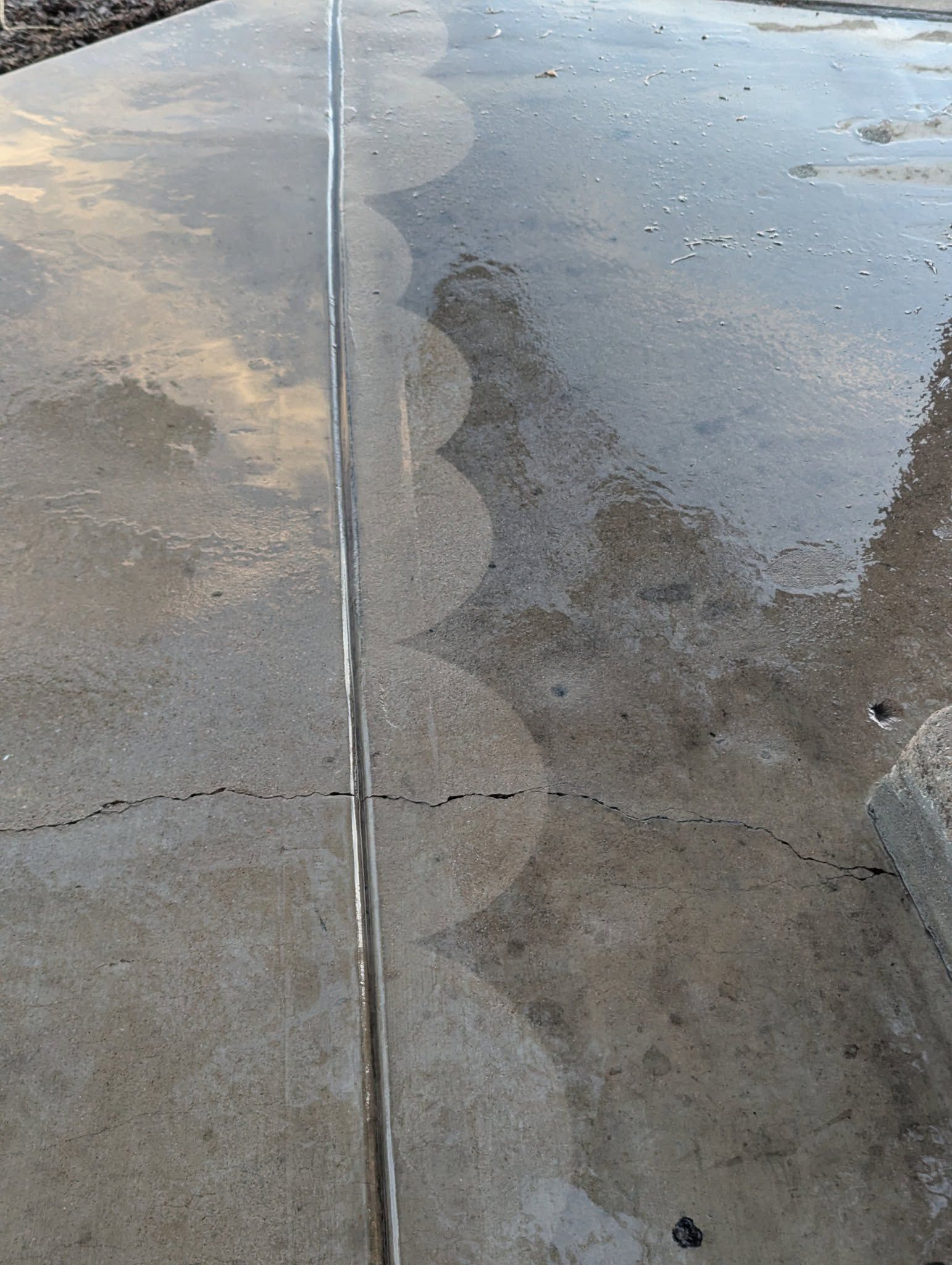 Wet concrete sidewalk with a long expansion joint and damp patches on both sides