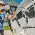 Person pressure-washing a white RV outdoors on a sunny day