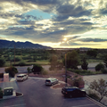 Sunset over mountains and a green valley, seen from a parking lot with several parked cars.