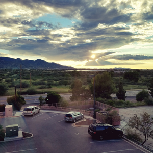 Sunset over mountains and a green valley, seen from a parking lot with several parked cars.