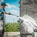 Worker pressure-washing a brick wall outdoors with a spray wand and water stream