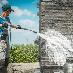 Worker pressure-washing a brick wall outdoors with a spray wand and water stream