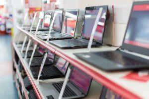 Rows of open laptops on shelves in a store display, with red and white shelving.