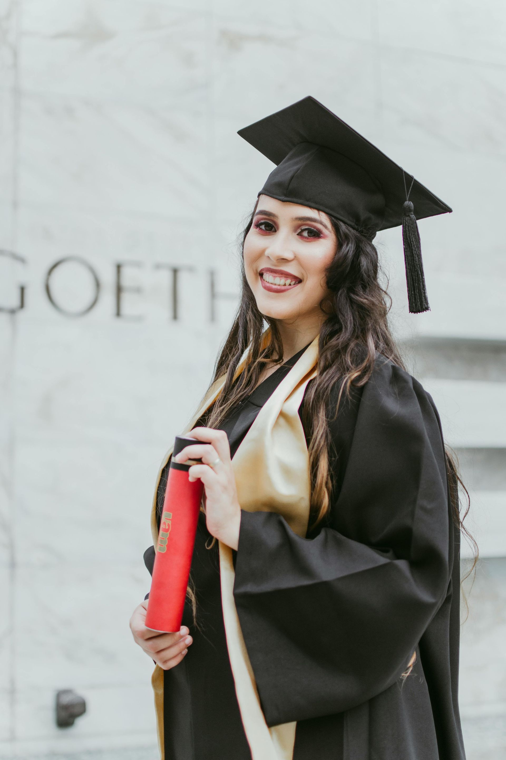 A woman in a graduation cap and gown is holding a diploma.