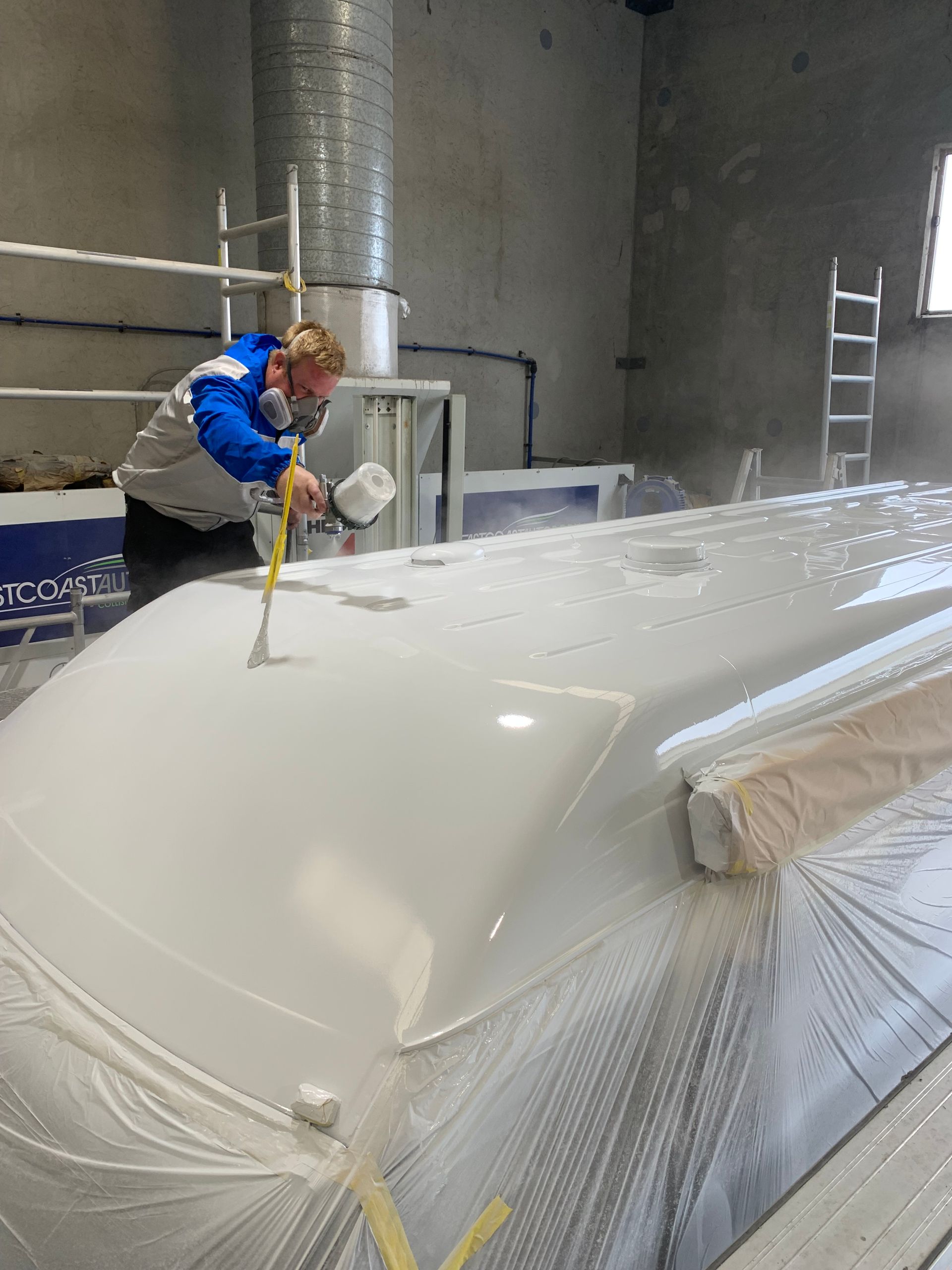 A man in a blue jacket is spray painting a white surface