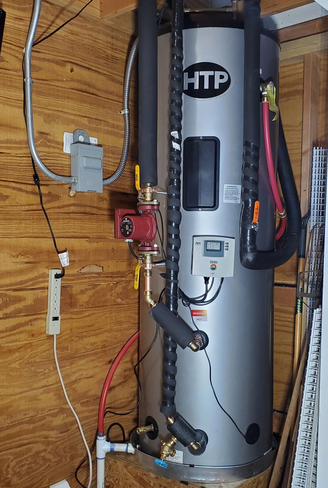 A htp water heater is hanging on a wooden wall.